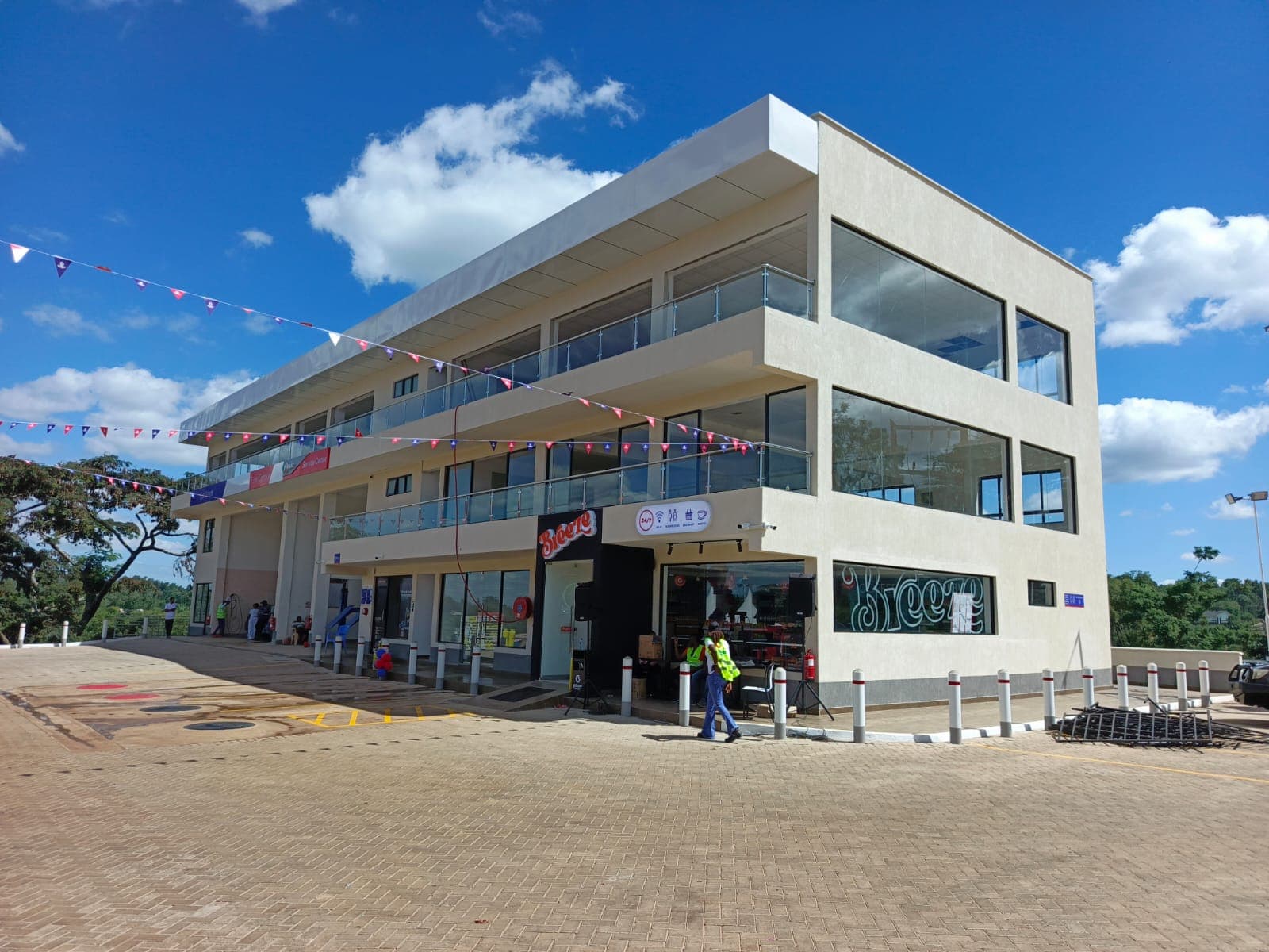 Retail frontage — ground-floor Breeze convenience store with full-height glazing, branded entrance, and paved customer circulation with safety bollards.